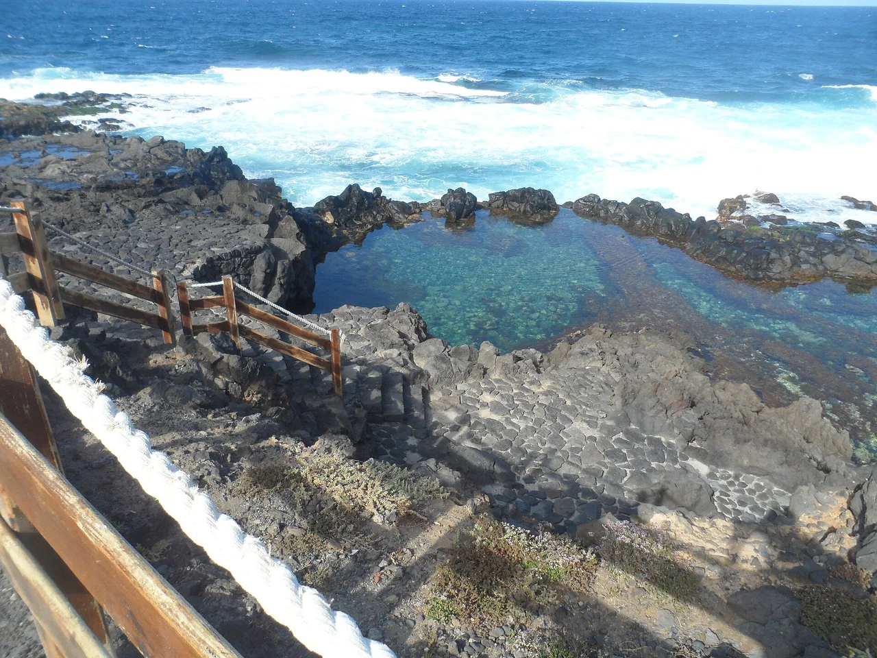 Vaso entre rocas oscuras con escalones y barandillas en el Charco de Los Chochos